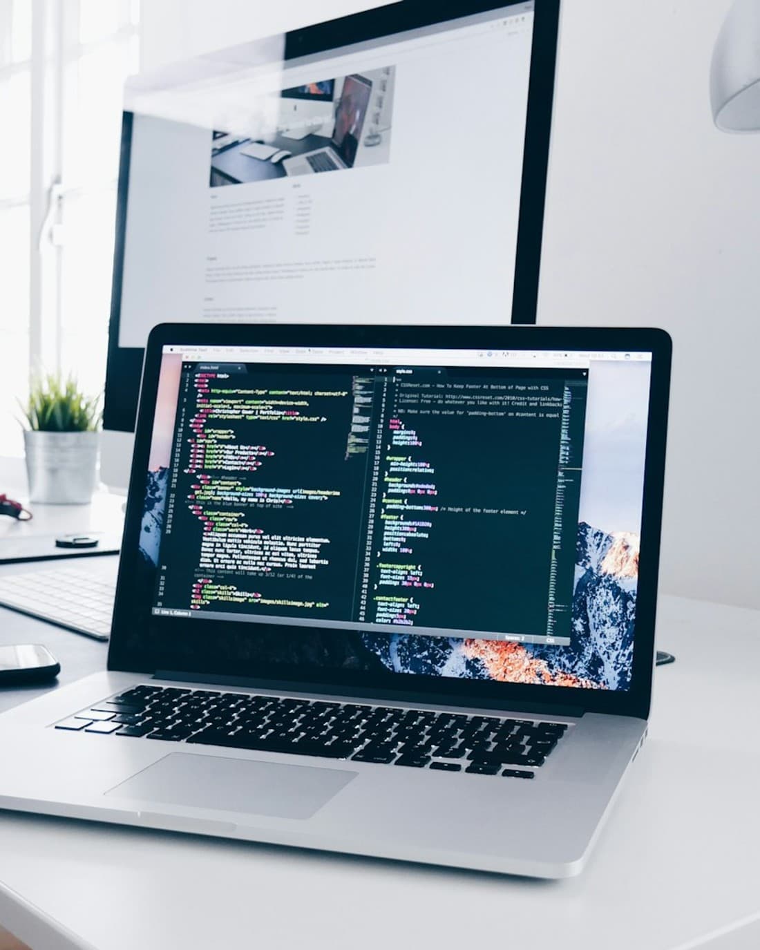 Portátil con código de una web abierto junto a un monitor con el diseño de la misma página